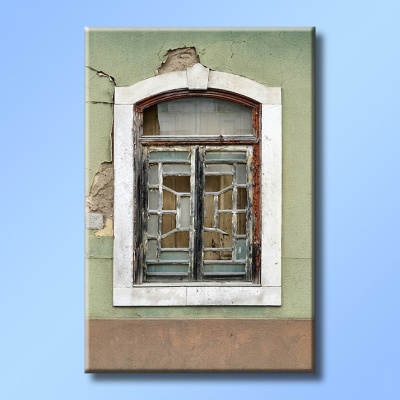 Imagem de uma janela antiga com vidros partidos numa parede verde clara com moldura branca