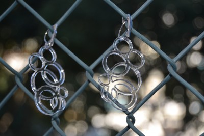 Dois pares de brincos prateados com anéis entrelaçados pendurados numa vedação metálica