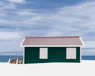 Casa pequena verde em madeira na praia com janelas cobertas e telhado vermelho