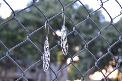 Brincos prateados de design em malha pendurados numa vedação metálica