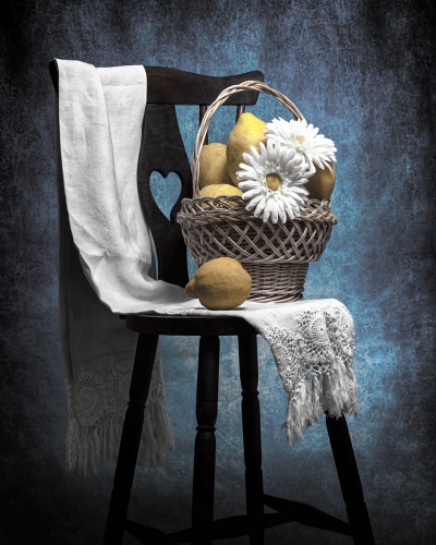 Cesto com peras e flores sobre cadeira de madeira preta com tecido branco