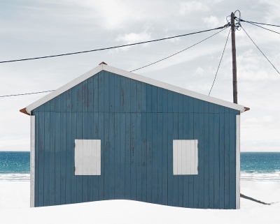 Casa de praia azul com janelas brancas em praia com areia branca e mar ao fundo