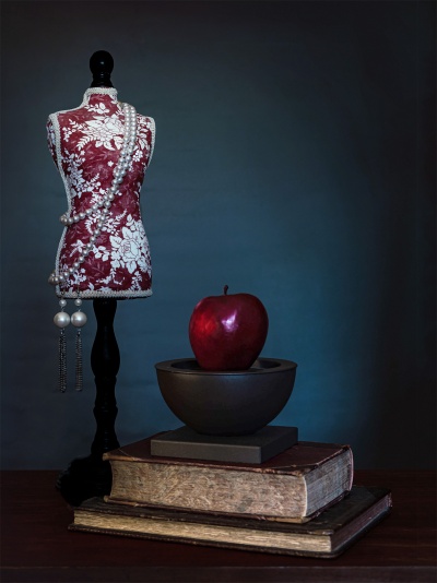 Maniquim decorativo com colar de pérolas, maçã vermelha em recipiente negro e livros antigos