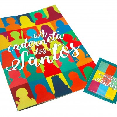 Caderno colorido com silhuetas e texto 'A caderneta dos Santos', com pacote pequeno ao lado