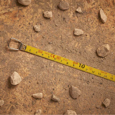 Fita métrica amarela sobre chão de terra com pedras pequenas