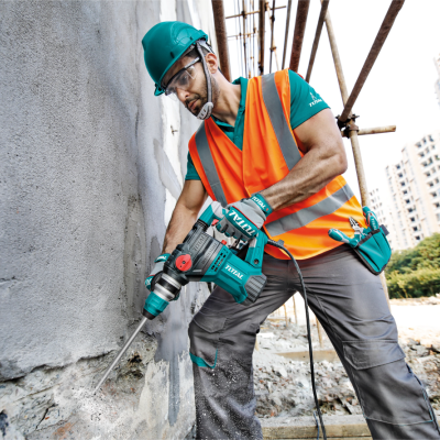 Trabalhador de construção com capacete e colete usando ferramenta elétrica TOTAL em parede de cimento