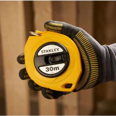 Fita métrica amarela Stanley de 30 metros segurada por mão enluvada em fundo de madeira
