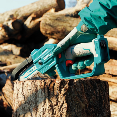 Mini motosserra TOTAL azul e cinza sobre tronco de madeira com mão luva azul