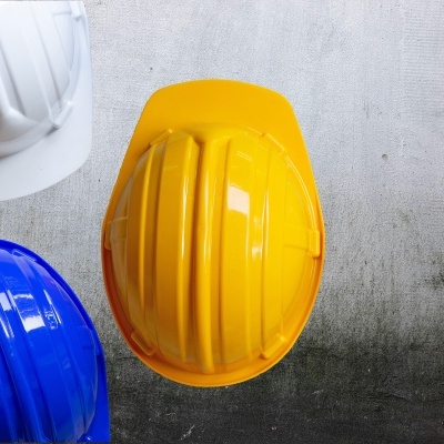 Três capacetes de segurança em plástico nas cores branca, amarela e azul sobre superfície cinzenta.
