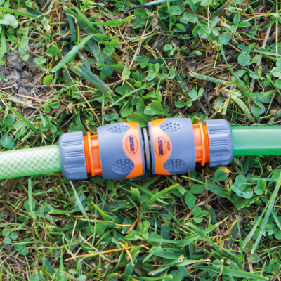 Conector de mangueira de jardim laranja e cinzento em duas mangueiras verdes sobre relva