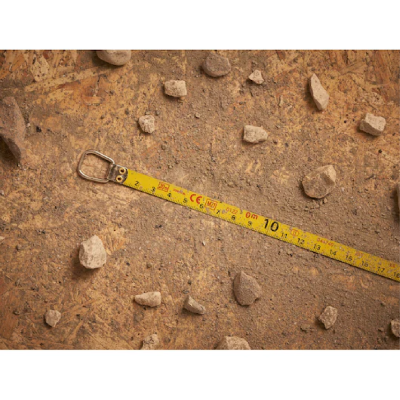 Fita métrica amarela no chão de terra com pedras