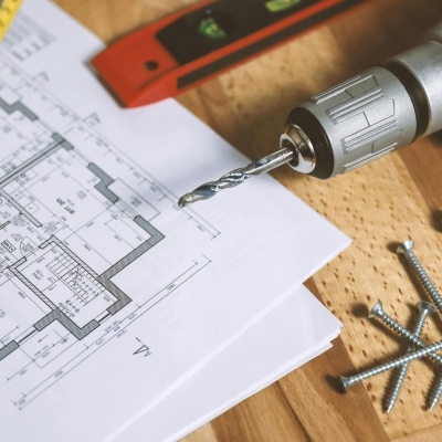 Broca metálica em broca elétrica com parafusos e planta arquitetónica sobre superfície de madeira