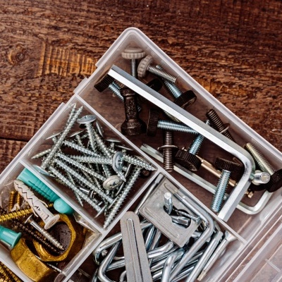 Caixa de plástico com parafusos, buchas, ganchos e chaves Allen sobre madeira