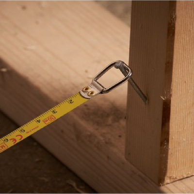 Fita métrica amarela pendurada num prego numa peça de madeira clara