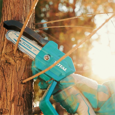 Mini motosserra elétrica TOTAL azul a cortar ramo fino de árvore com mão com luva azul ao pôr do sol
