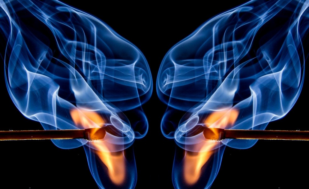 Dois fósforos acesos com chamas laranja e fumo azul em fundo preto