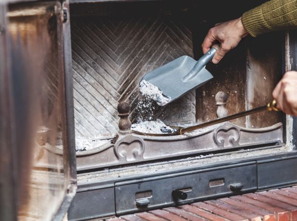 Pessoa limpando cinzas de lareira com pá e ferramenta