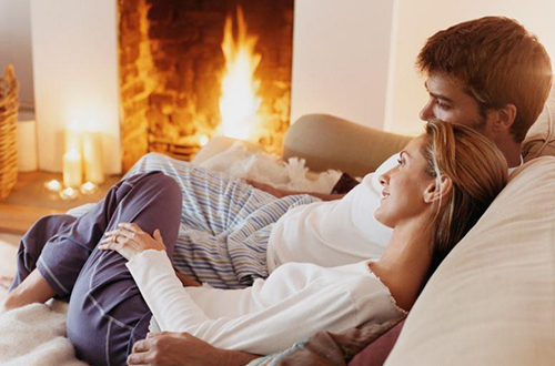 Casal sentado no sofá perto da lareira acesa num ambiente acolhedor