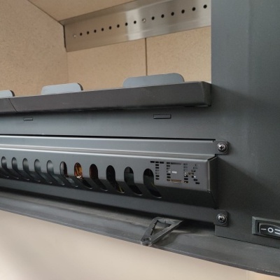 Equipamento eletrónico cinzento com botão de ligar/desligar e grelha de ventilação numa superfície clara