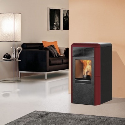 Lareira moderna em metal vermelho e preto com chama visível numa sala com cadeira preta, mesa e candeeiro