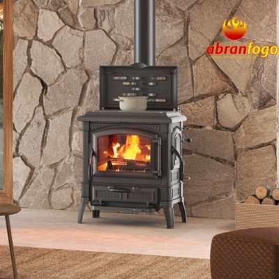 Lareira a lenha preta em ferro fundido com fogo aceso, parede de pedra e caixa de lenha ao lado