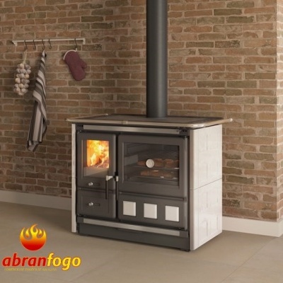 Fogão a lenha com chama visível, cerâmica branca e fundo de tijolo rústico