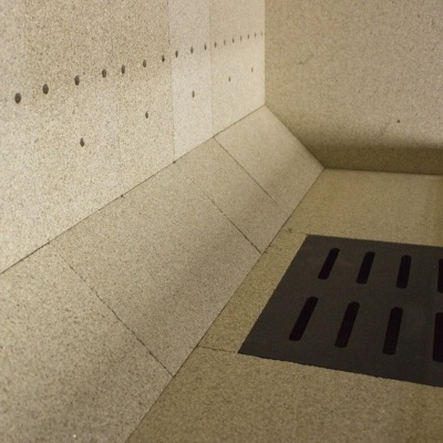 Dreno de chão preto embutido em pavimento e parede de pedra cinzenta