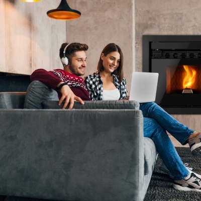 Casal sentado em sofá cinza perto de salamandra a lenha embutida com fogo visível