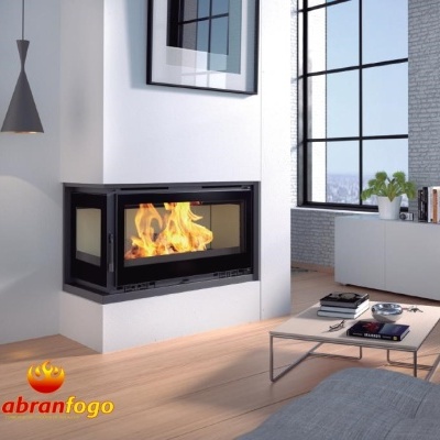 Lareira embutida com estrutura preta e vidro mostrando chamas numa sala moderna com chão em madeira clara e móveis brancos