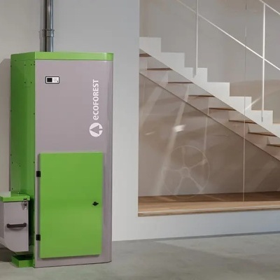 Caldeira de biomassa verde e cinza numa garagem com carro cinza e escada branca ao fundo