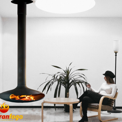 Lareira suspensa preta com fogo numa sala branca minimalista com pessoa sentada e planta