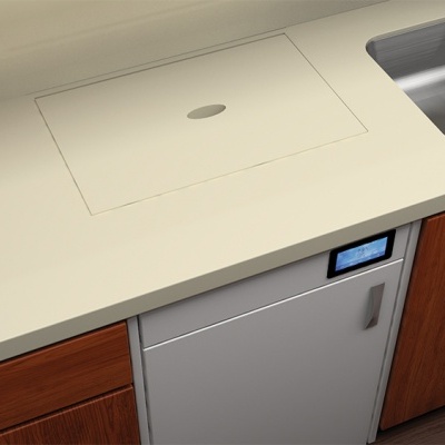 Eletrodoméstico embutido prateado com ecrã digital azul entre armários de madeira e tampo de cozinha bege.