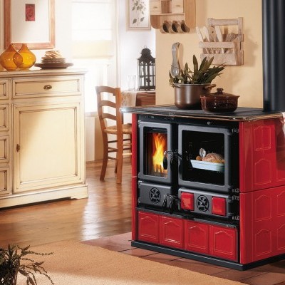 Fogão a lenha vermelho e preto com cozinha ao fundo em madeira clara