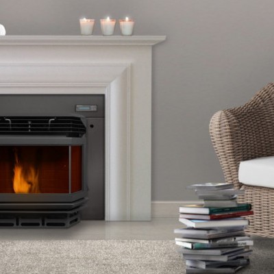 Lareira elétrica preta com moldura branca, cadeira de vime castanha com almofada branca e pilha de livros sobre tapete cinza