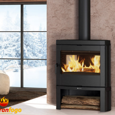 Lareira a lenha em metal preto com madeira e janela nevada ao fundo