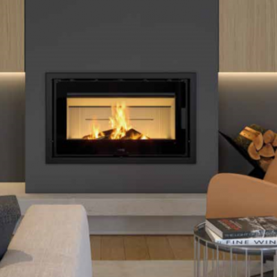 Lareira embutida com moldura preta numa parede cinza escuro, sofá cinza, poltrona laranja, mesa baixa preta com livros e chão de madeira.