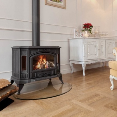 Lareira a lenha com vidro frontal, suporte para lenha e mobiliário clássico numa sala clara.