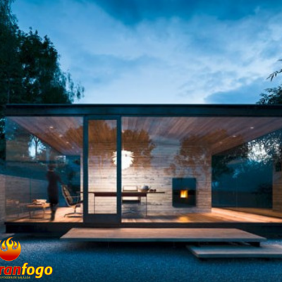 Casa moderna em vidro e madeira com lareira e ambiente exterior natural ao entardecer