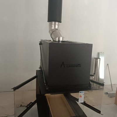 Lareira metálica preta com tubo de fumo instalada no interior com paredes brancas e chão cinza