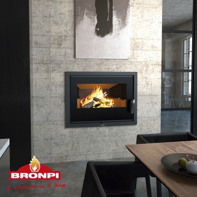 Lareira embutida em metal preto numa parede de cimento aparente com mesa de madeira e cadeiras pretas ao lado