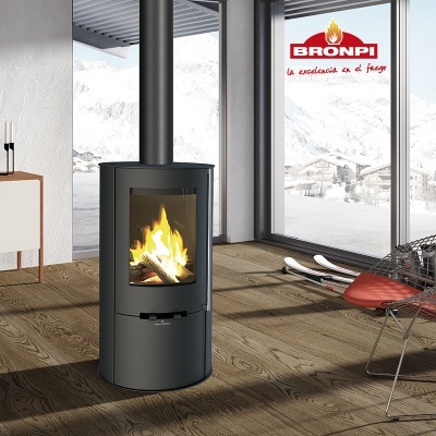 Lareira preta redonda com fogo aceso perto de janela grande com vista de neve