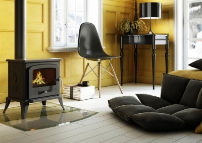 Sala com cadeira preta, lareira a lenha, mesa de apoio, sofá cinzento e paredes amarelas