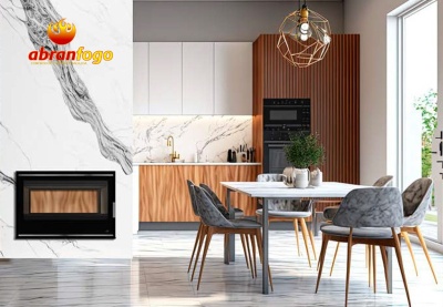 Cozinha moderna com armários em madeira clara, lareira embutida preta, mesa branca com cadeiras cinza e luminária dourada