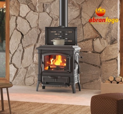 Lareira a lenha preta em ferro fundido com fogo aceso, parede de pedra e caixa de lenha ao lado