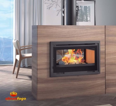 Lareira fechada embutida em madeira clara com fogo visível, cadeira clara e cortinas ao fundo