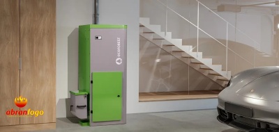 Caldeira de biomassa verde e cinza numa garagem com carro cinza e escada branca ao fundo