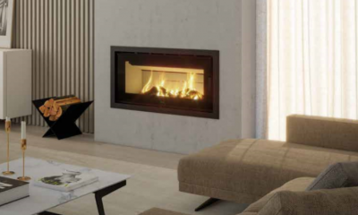 Lareira moderna embutida numa parede cinzenta com fogo visível e suporte de madeira preta.