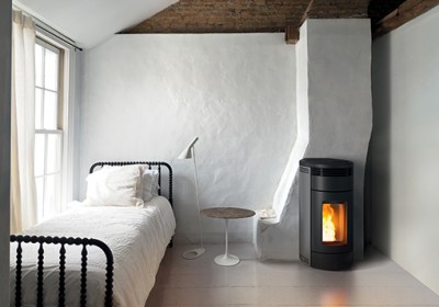 Quarto com cama metálica preta, a roupa de cama branca, luminária de pé, mesa lateral redonda e lareira moderna preta.