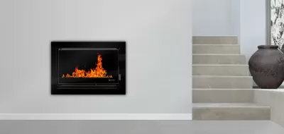 Lareira elétrica embutida com moldura preta e chamas laranjas numa parede branca ao lado de escadas e vaso decorativo.
