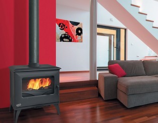 Lareira a lenha preta junto a parede vermelha num espaço com sofá e escada